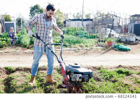 Man professional gardener using plow at land with green grass in garden Man professional gardener using plow at land with green grass in garden 68124141