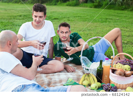 Three adult men enjoying picnic outdoors on summer day 68124142