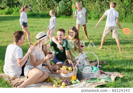Four adult people on picnic outdoors and children playing Four adult people on picnic outdoors and children playing 68124143