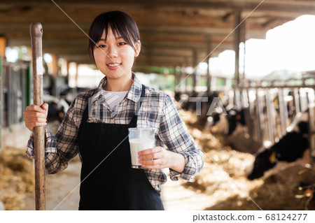Young positive female dairy farm worker standing with glass of fresh milk 68124277