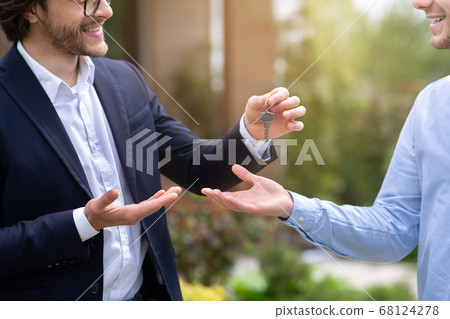 Cropped view of real estate agent giving house key to new home owner near his property, close up Cropped view of real estate agent giving house key to new home owner near his property, close up 68124278