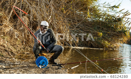 Fisherman sitting on stool and pulling fish Fisherman sitting on stool and pulling fish 68124280