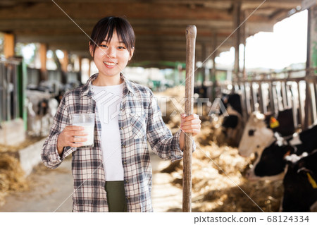 Cheerful woman is holding glass of milk at the cow farm Cheerful woman is holding glass of milk at the cow farm 68124334