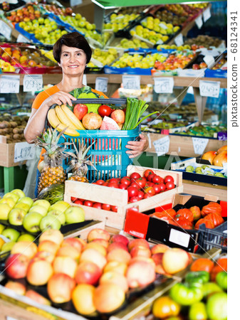 Smiling female is standing with basket with vegetables and fruits Smiling female is standing with basket with vegetables and fruits 68124341