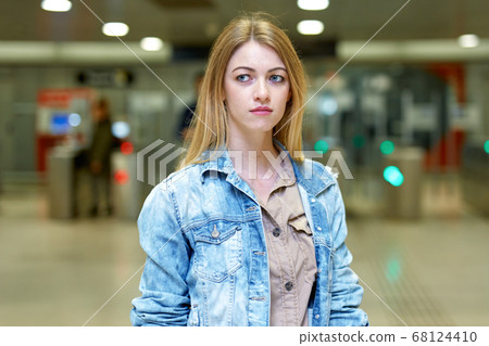 Blonde with long hair stands near the turnstiles at subway station 68124410