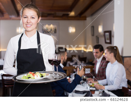Young waitress with serving tray meeting restaurant guests 68124628