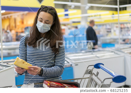 woman in protective medical mask in a supermarket chooses cheese. pandemic and covid-19 concept. Hand of the buyer with a piece of cheese in the store. toned woman in protective medical mask in a supermarket chooses cheese. pandemic and covid-19 concept. Hand of the buyer with a piece of cheese in the store. toned 68125235
