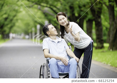 A smiling senior couple with a man sitting in a wheelchair and a woman snuggling up to him A smiling senior couple with a man sitting in a wheelchair and a woman snuggling up to him 68125254