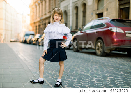 Full length portrait of beautiful little blond girl outdoors at old city street in Lviv, Ukraine. Fashion strret portrait of pretty girl in the city 68125973