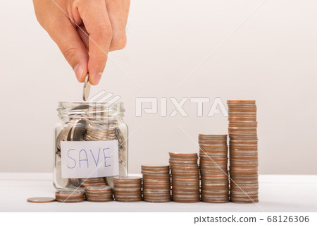 Hand of male putting coins in jar with money stack 68126306