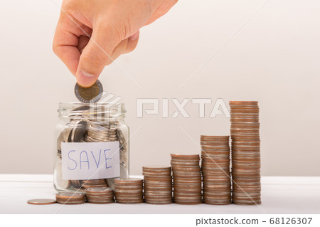 Hand of male putting coins in jar with money stack 68126307