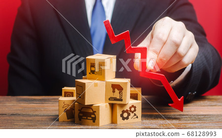 Businessman holds a red down arrow over the boxes. Business industrial production drop rate. Shortage of products. Low supply and demand, falling market recession, low delivery volumes. Overproduction 68128993