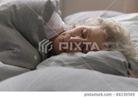Elderly woman sleeping in bed under blanket in cozy bedroom 68130569