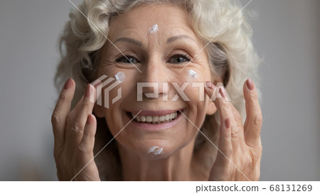 Closeup senior woman applying effective facial cream feels happy Closeup senior woman applying effective facial cream feels happy 68131269