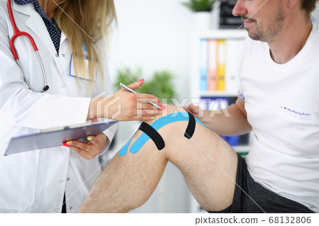 Doctor examines an injured knee in patient with kinesio tape Doctor examines an injured knee in patient with kinesio tape 68132806