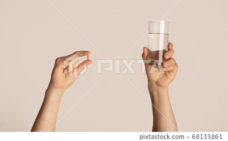 Cropped view of millennial guy holding glass of water and pill on light background, closeup 68133861