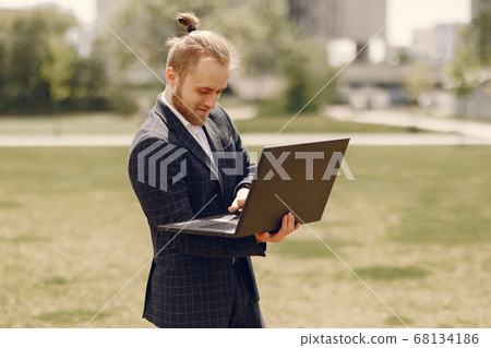 Businessman with laptop in a summer city Businessman with laptop in a summer city 68134186