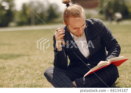 Businessman with book sitting in a summer city 68134187
