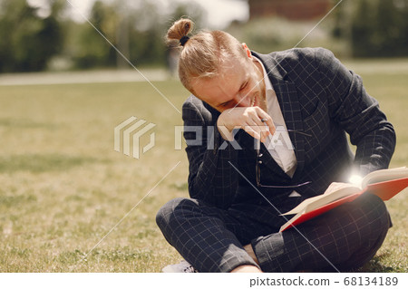 Businessman with book sitting in a summer city Businessman with book sitting in a summer city 68134189