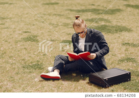 Businessman with book sitting in a summer city Businessman with book sitting in a summer city 68134208