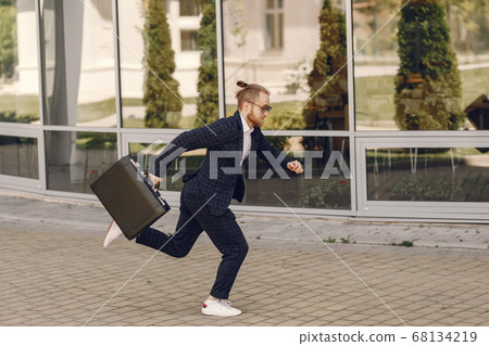 Businessman with suitcase walking in a summer city Businessman with suitcase walking in a summer city 68134219