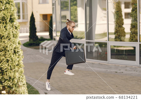 Businessman with suitcase walking in a summer city Businessman with suitcase walking in a summer city 68134221