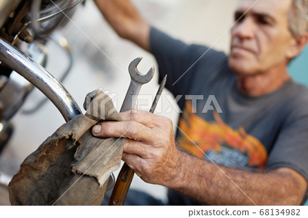 Senior Man Examining His Motorcycle And Fixing Engine Senior Man Examining His Motorcycle And Fixing Engine 68134982