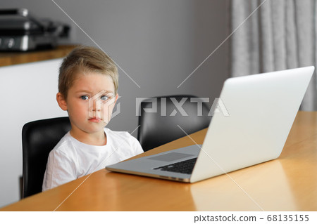 A young boy using a laptop computer sitting on top of a table at home 68135155