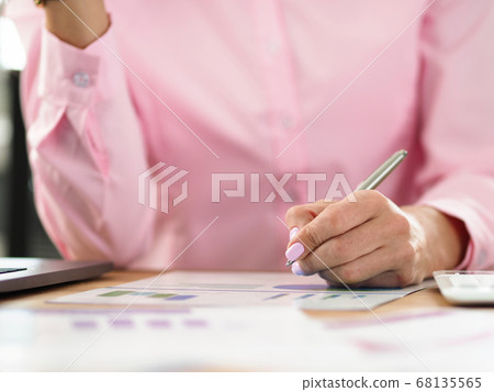 Woman sits at workplace and takes notes on chart 68135565