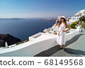 Female In a white dress posing against the backdrop of the city of Thira, Santorini. 68149568