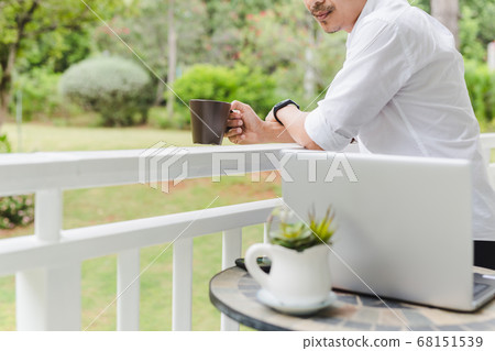 Businessman relax standing on terrace hand holding coffee with laptop on table. Businessman relax standing on terrace hand holding coffee with laptop on table. 68151539