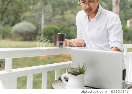 Businessman in glasses holding coffee while working on laptop. 68151542