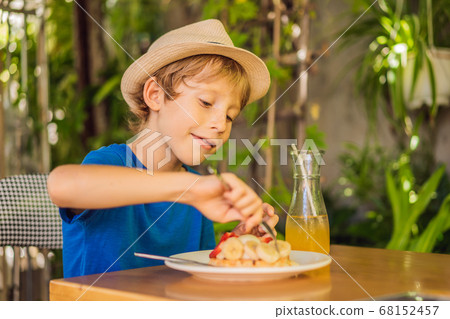 A little boy eats dessert Belgian waffles with strawberry in a cafe A little boy eats dessert Belgian waffles with strawberry in a cafe 68152457