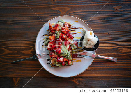 Tasty and colorful Belgian Waffle with fruites and chocolate on wooden table Tasty and colorful Belgian Waffle with fruites and chocolate on wooden table 68153188