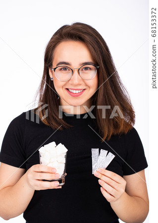 young beautiful woman in glasses with a smile, holds in one hand a glass of white sugar, in the other hand a plate of chewing gum young beautiful woman in glasses with a smile, holds in one hand a glass of white sugar, in the other hand a plate of chewing gum 68153372
