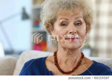 Slender elderly woman sits on sofa in an apartment Slender elderly woman sits on sofa in an apartment 68154397