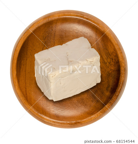 Fresh bakers yeast block in a wooden bowl. Compressed fresh yeast, used in baking as leavening agent to convert sugars in dough to carbon dioxide. Saccharomyces cerevisiae. Close-up from above, photo. 68154544