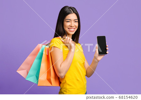 Online Shopping. Happy Asian Girl With Shopper Bags Demonstrating Black Smartphone Screen Online Shopping. Happy Asian Girl With Shopper Bags Demonstrating Black Smartphone Screen 68154620