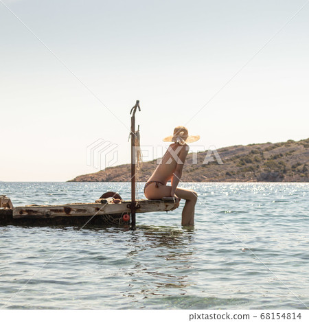 View of unrecognizable woman wearing big summer sun hat tanning topless and relaxing on old wooden pier in remote calm cove of Adriatic sea, Croatia View of unrecognizable woman wearing big summer sun hat tanning topless and relaxing on old wooden pier in remote calm cove of Adriatic sea, Croatia 68154814