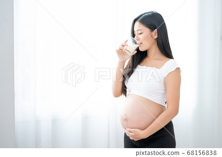 Close up beautiful Asian pregnant woman is drinking milk and stand in front of white curtain Close up beautiful Asian pregnant woman is drinking milk and stand in front of white curtain 68156838