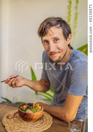 Man eating Poke bowl with shrimp, corn, avocado, ginger and mushrooms Man eating Poke bowl with shrimp, corn, avocado, ginger and mushrooms 68156875