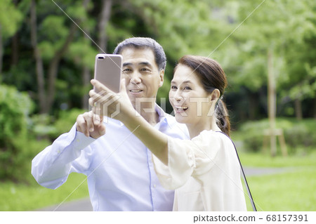A smiling senior couple taking pictures with their smartphones 68157391