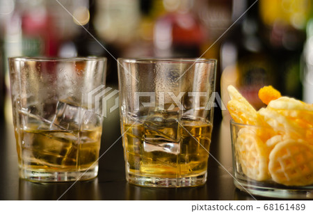glass of whiskey with ice cubes and salty snacks 68161489