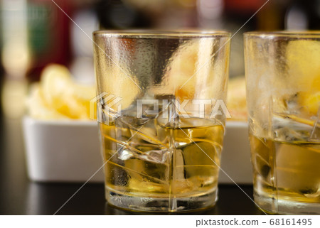 glass of whiskey with ice cubes and salty snacks 68161495