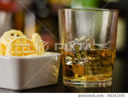 glass of whiskey with ice cubes and salty snacks 68161505