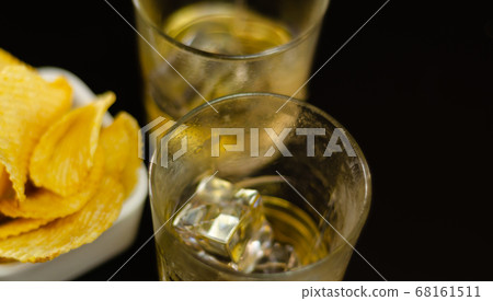 glass of whiskey with ice cubes and salty snacks 68161511