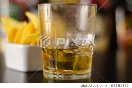 glass of whiskey with ice cubes and salty snacks 68161522
