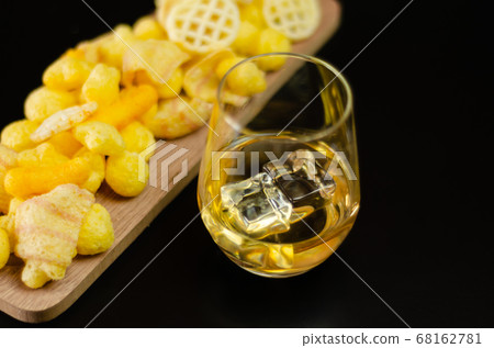 glass of whiskey with ice cubes and salty snacks 68162781
