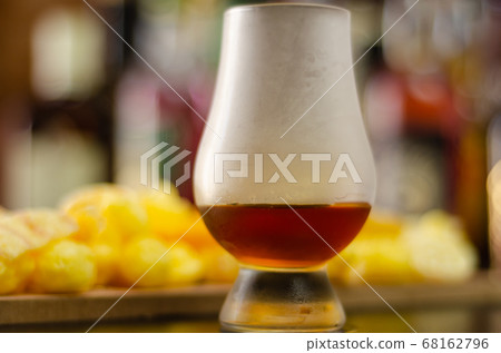 glass of whiskey with ice cubes and salty snacks 68162796