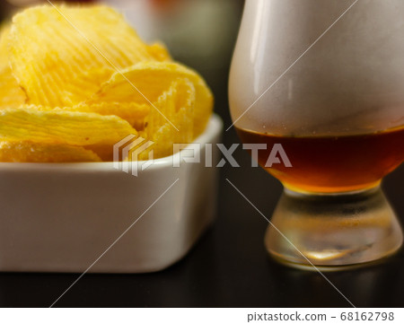 glass of whiskey with ice cubes and salty snacks 68162798